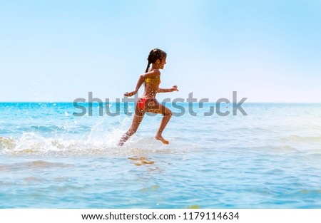 Summer fun beach woman splashing water. Panorama landscape of tropical ocean on travel holiday. Bikini girl running in freedom and joy with hands up enjoying the sun.
