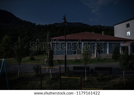 Mountain night landscape of building at forest at night with moon or vintage country house at night with clouds and stars. Summer night. Photo taken with long exposure