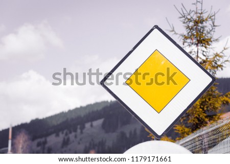 Blank yellow road sign meaning " Yield pedestrians " and "Main high  priority road" on sky background in nature, forest mountains. Safety concept in rural ambience out of town 