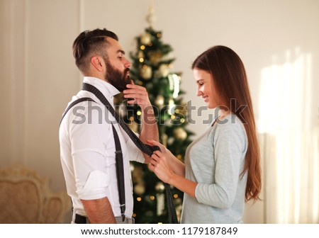 Woman clothe her boyfriend tie on the background Christmas tree at home 