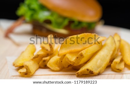 Crispy golden deep fried potato chips or French fries served with a burger on a wooden board, close up view