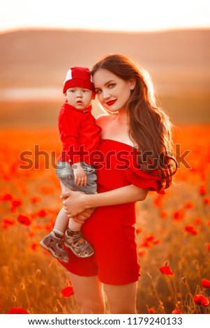 Mother with son in poppies enjoying life at sunset. Happy family summer vacation. Pretty brunette with long healthy hair holding little boy. Carefree young mom over red field. Countryside landscape.