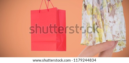 Elegant woman holding shopping bag against orange background 