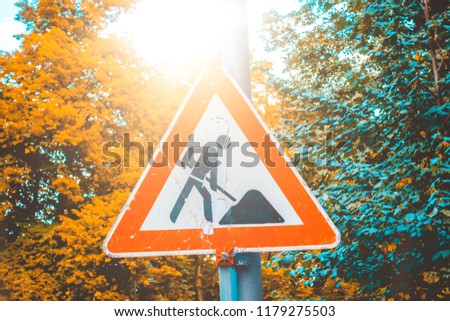 building site traffic sign as red triangle with some colorful trees in the background