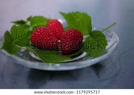 Ripe red berries raspberries on a plate with green leaves 
