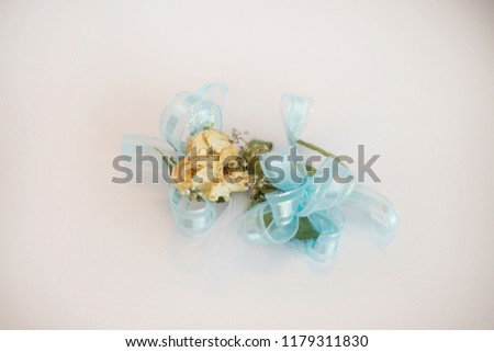 Rose wrist corsage with blue ribbon on white background.