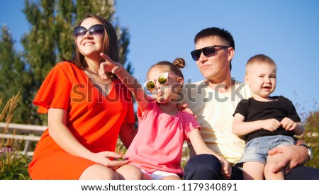Beautiful happy family. They sit on a park bench, sunglasses. Little daughter pointing her finger at the sky
