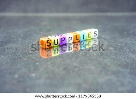 Conceptual of supplies as balance sheet under financial spelled on colorful alphabet beads. Isolated over reflective dark surface. Focus on selective beads in foreground; other in gradient blur.