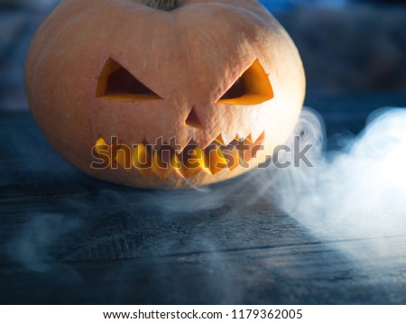 Crazy pumpkin monster on Halloween looks through the smoke. Close - up of scary orange pumpkin face