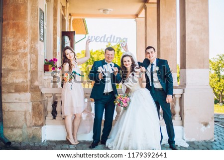 Newlywed couple, bridesmaids & groomsmen having fun outdoors before wedding ceremony. Bride and groom and friends hold in hand wooden wedding decoration with words "Wedding"
