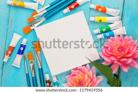 summer background. dahlias, paints, brushes and a canvas on a blue wooden background. art. space for a text