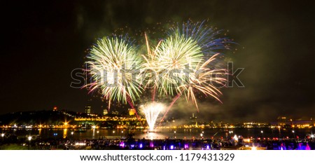 Bright green and orange/red fireworks over the Saint-Lawrence River near Quebec City during a Canadian summer festival.