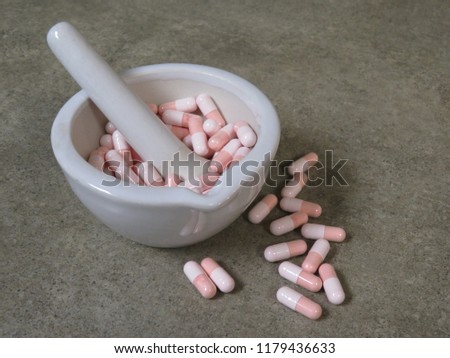 Pink and white gelatin capsules in a white, ceramic (wedgewood) mortar with pestle on a compounding pharmacy countertop.