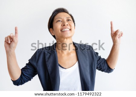 Smiling Asian woman pointing and looking upwards. Positive young lady. Promotion concept. Isolated front view on white background.