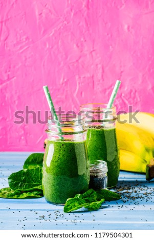 Green smoothies in glass bottles on cool pink blue background with yellow bananas, selective focus