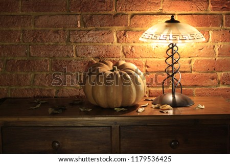 Portrait of a pumpkin on an antique piece of furniture during the night time with a lamp that illuminates it. concept: Halloween, horror, scary