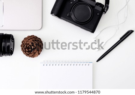 Top view of a desk working with laptop keyboard, modern camera, lens, headphones, notes writing a black pen on a white background. Freelance, creative or online education concept.