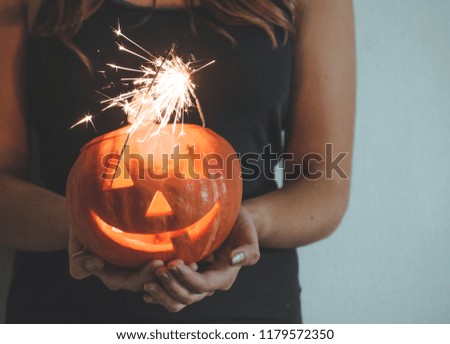 Halloween pumpkin in the hands of a girl with Bengal lights. Holiday Halloween concept. Beautiful woman with pumpkins