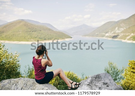 Young tourist Girl taking pictures of mountains and lake. Georgia. Summer. August. Girl making a photo shoot of mountain. Zhinvali reservoir.