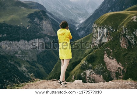 A young Girl in a yellow raincoat tourist photographs the mountains. Girl making a photo shoot of mountain. Georgia. Summer. August. 