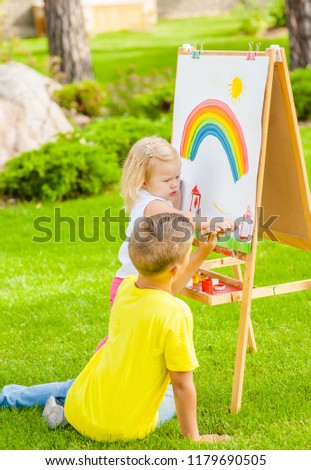 Children drawing with colorful paints in summer park. Creative child painting on nature. Talented toddler painter.