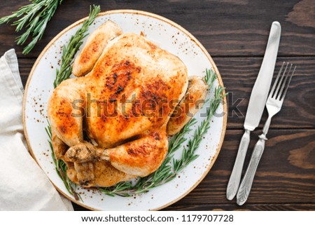 Whole grill chicken with caramelized skin and fresh rosemary on a wooden dinner table.