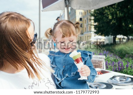 Portrait of a young mother and her 3 years old daughter eating ice cream in a city park on a warm sunny day