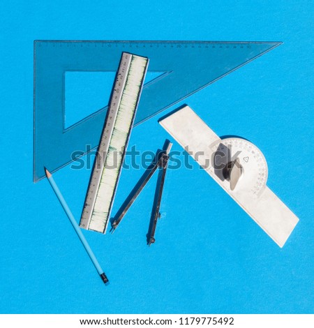 Geometry set with compass, rulers, pencil and protractor on blue background - top view
