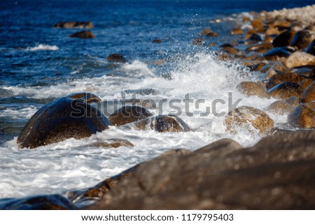 Close-up of sea water blue wave is beating against stones, spray.