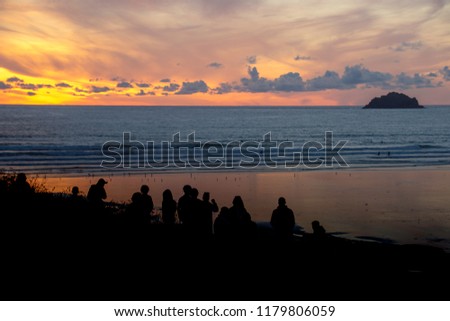 Silhouettes of people watching the sunset over Polzeath surfing beach North Cornwall, UK