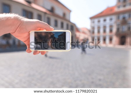 Tourist photographs the street of the old town on the camera of the smartphone. Phone is close-up and in focus.
