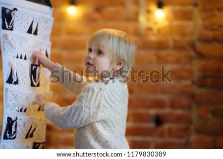 Happy little boy takes sweet from advent calendar on Christmas eve. Traditional christmas calendar for kids