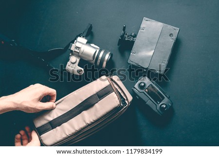 overhead top view of hand put camera accessories in the bag on dark background
