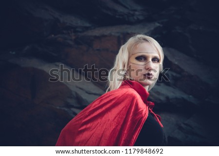 woman in superhero outfit wearing bright red cape and golden mask with stone ceiling in background