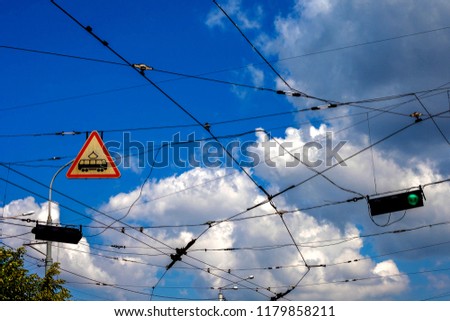 sign of a tram, trolley lines and a green traffic light against a blue cloudy sky