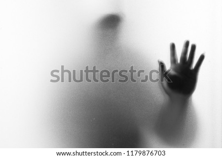 Shadow blur of horror man.Hands on the glass.Dangerous man behind the frosted glass.Mystery man.Halloween background.Black and white picture.Blur picture Royalty-Free Stock Photo #1179876703
