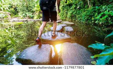 Male hiker with backpack crossing a river on stones. Royalty-Free Stock Photo #1179877801