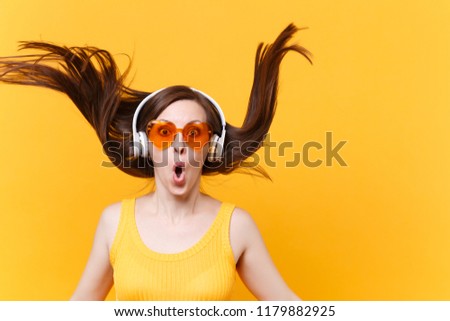 Portrait of excited cheerful laughter funny comic woman in orange glasses in headphones with fluttering hair isolated on yellow background. People sincere emotions lifestyle concept. Advertising area