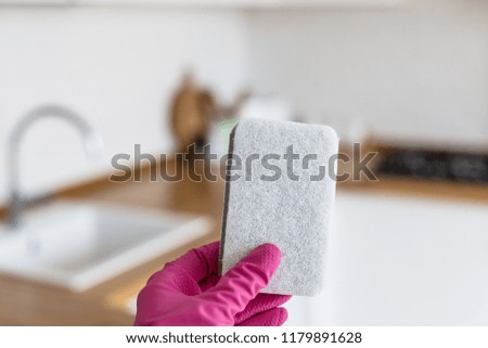 Woman hands wearing protective gloves and holding cleaning sponge on white kitchen background. Concept of clean kitchen