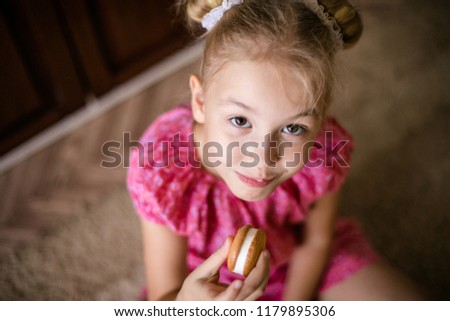Blonde brown-eyed girl eats sweet biscuit.