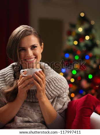 Happy young woman with cup of hot chocolate in front of Christmas lights