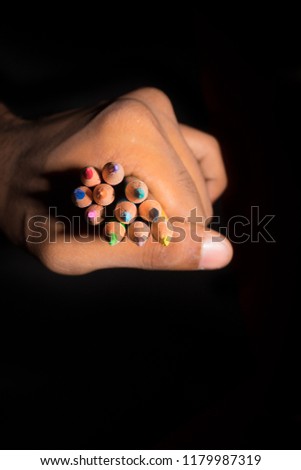 Close up of artist hand holding showing colorful sketch pencils on isolated black background. Abstract education design and creativity concept. Vertical copy space. 