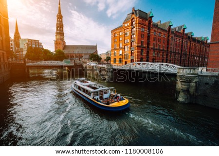 Touristic cruise boat on a channel with bridges in the old warehouse district Speicherstadt in Hamburg in golden hour sunset light, Germany Royalty-Free Stock Photo #1180008106