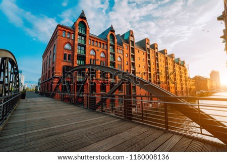 Pedestrian arch bridge over canals in the Speicherstadt of Hamburg. Warm golden hour sunset light on red bricks buildings Royalty-Free Stock Photo #1180008136