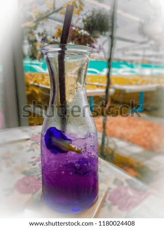 Selective focused of butterfly pea juice in the long glass with the flower inside placed on the table with blurred background and summer light in the afternoon