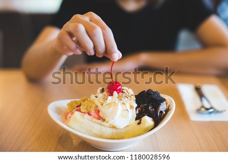 Female hand putting red cherry on sweet homemade banana split sundae. Royalty-Free Stock Photo #1180028596