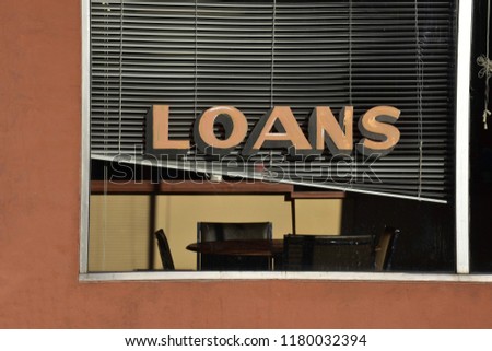 Loans office storefront on a main street in a small town, showing open, offset  venetian blinds, a table with chairs, and a shadow.