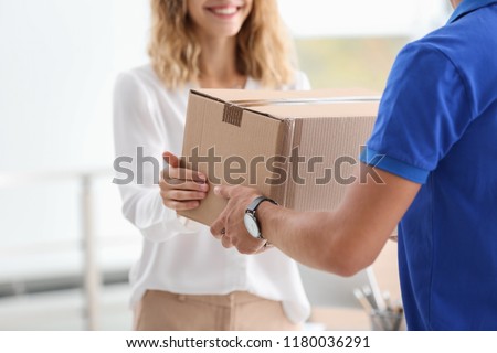 Young woman receiving parcel from courier indoors Royalty-Free Stock Photo #1180036291
