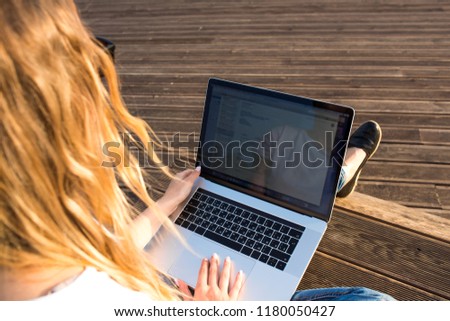 Female skilled website content creator distance working on laptop computer, sitting outdoors in sunny day.Woman having online training course via notebook.Searching information on web site via netbook