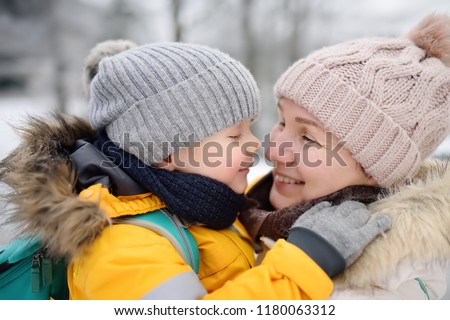 Mother or grandmother with her little son or grandson embrace and having fun together in snowy winter day